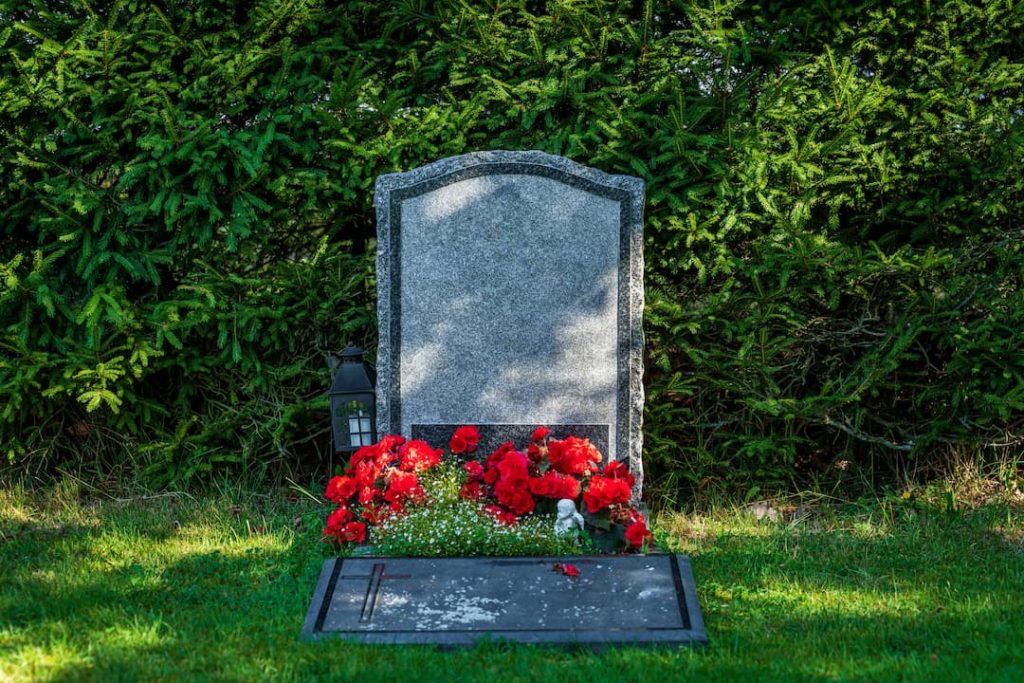 Headstone With Red Flowers On With Greenery In The Background